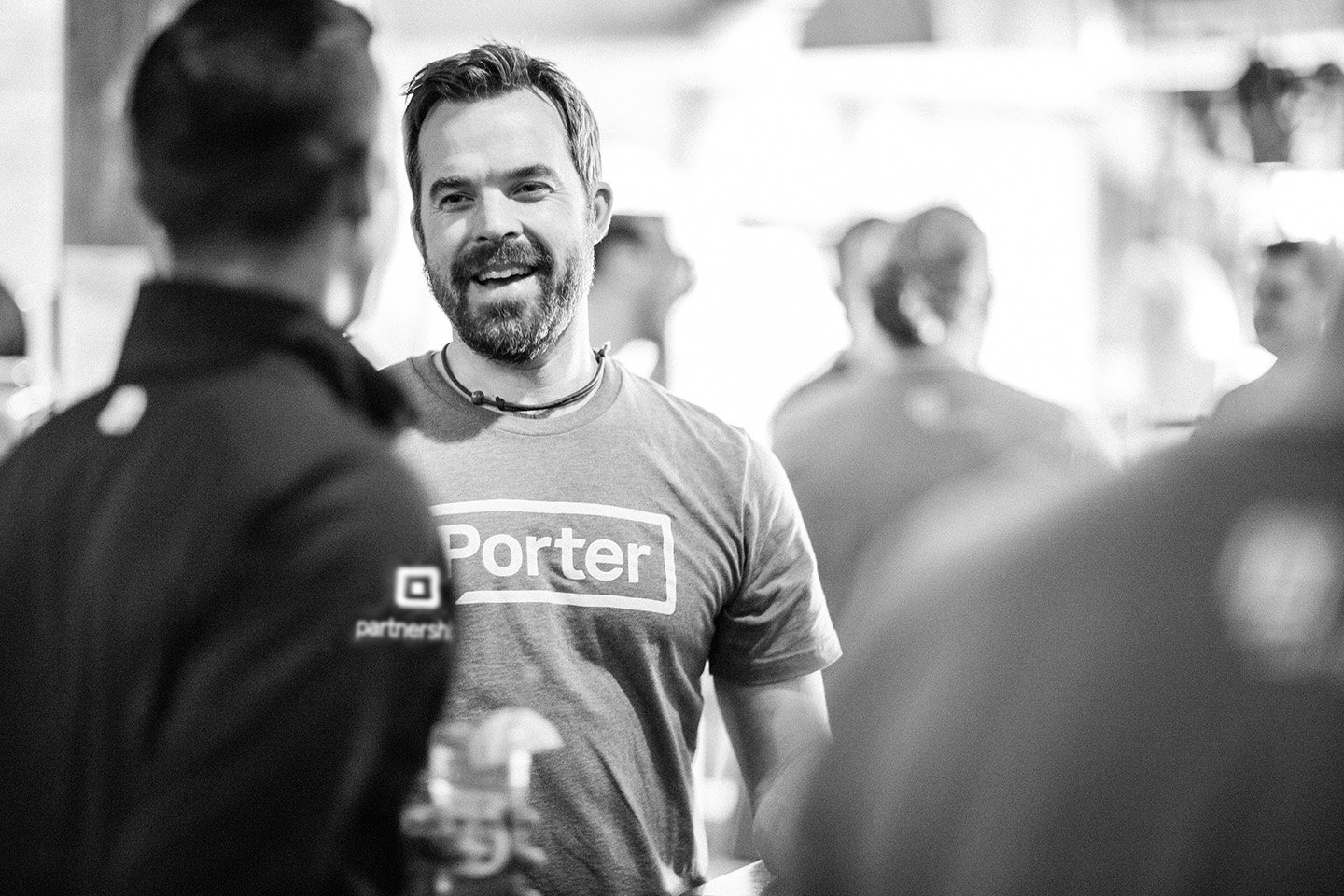 Smiling bearded man in a "Porter" t-shirt chatting at a gathering, black and white