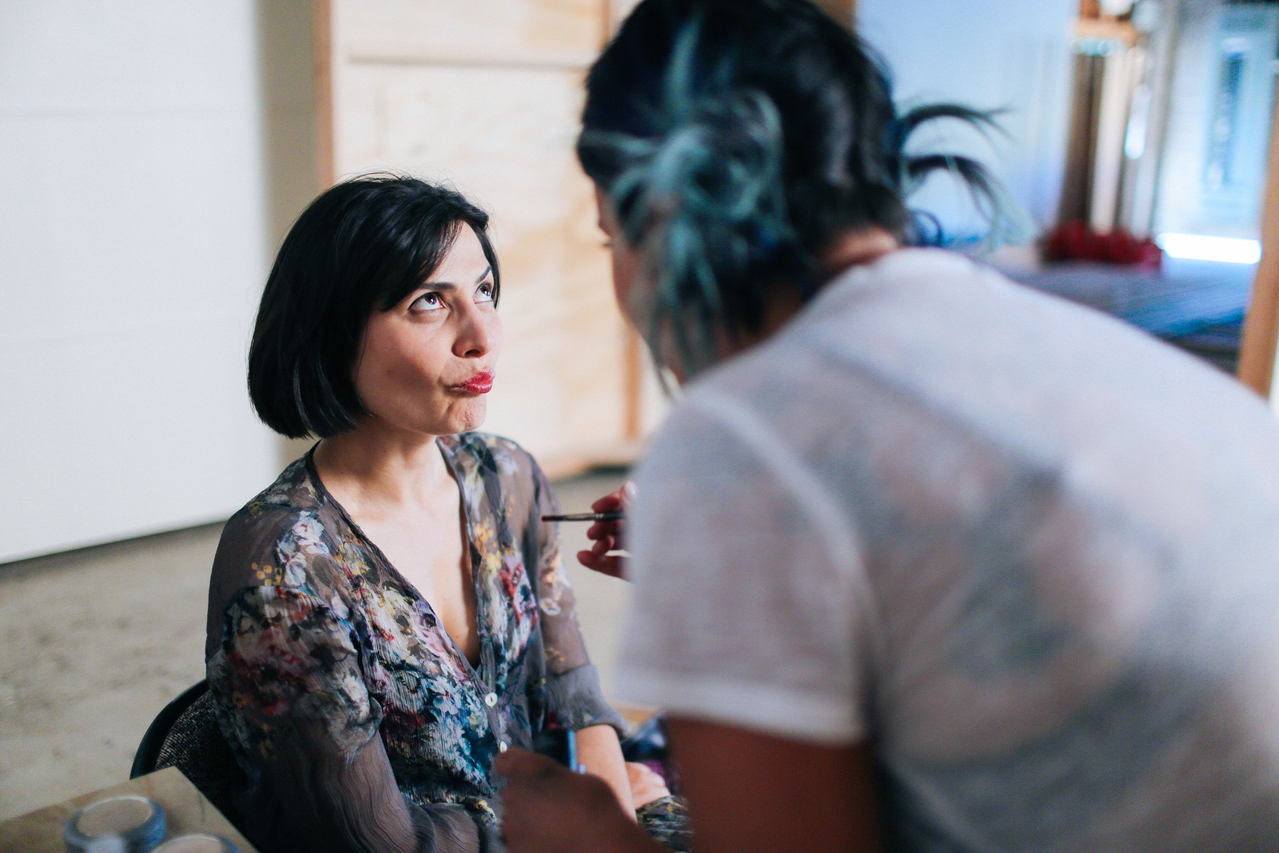 Makeup artist with teal hair applying lipstick to a seated woman at a WSECU shoot