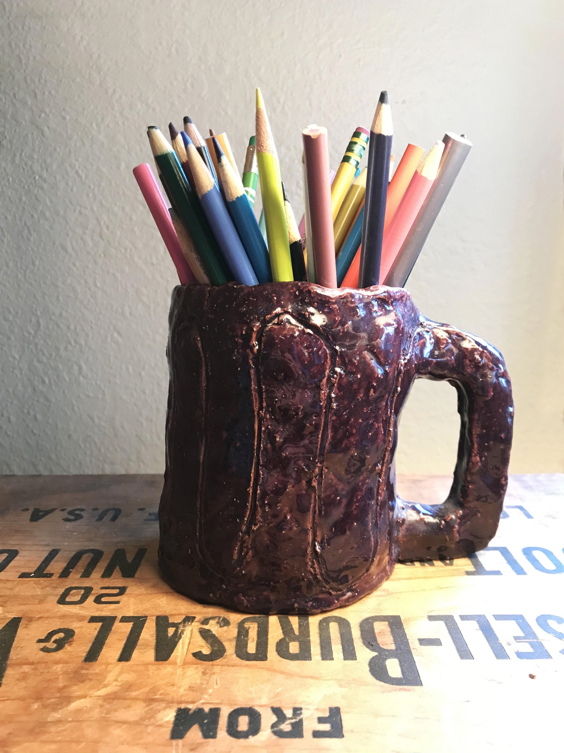 Handmade glazed ceramic mug holding colored pencils on a vintage wooden crate