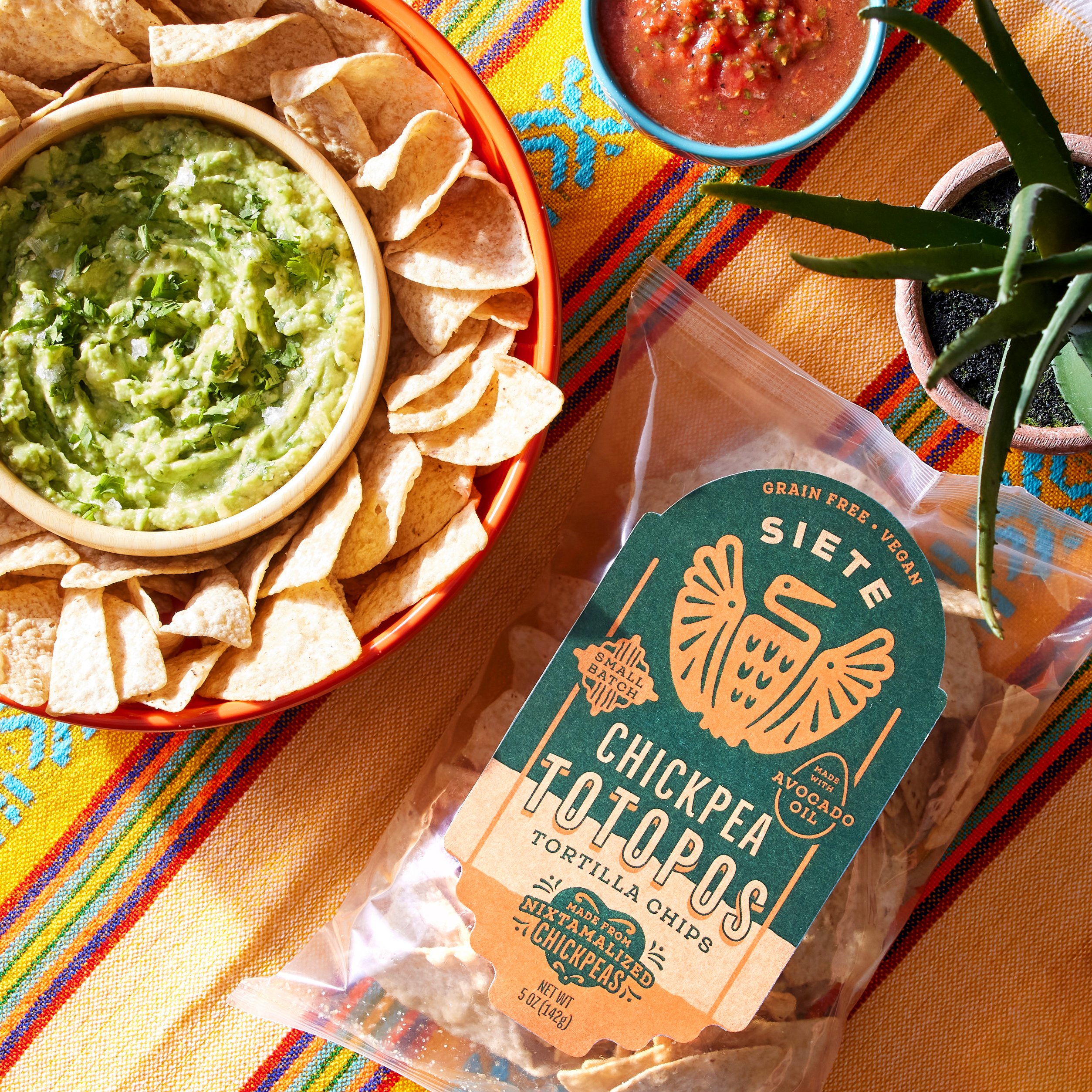 Siete Chickpea Totopos chips bag with guacamole and salsa on a striped textile