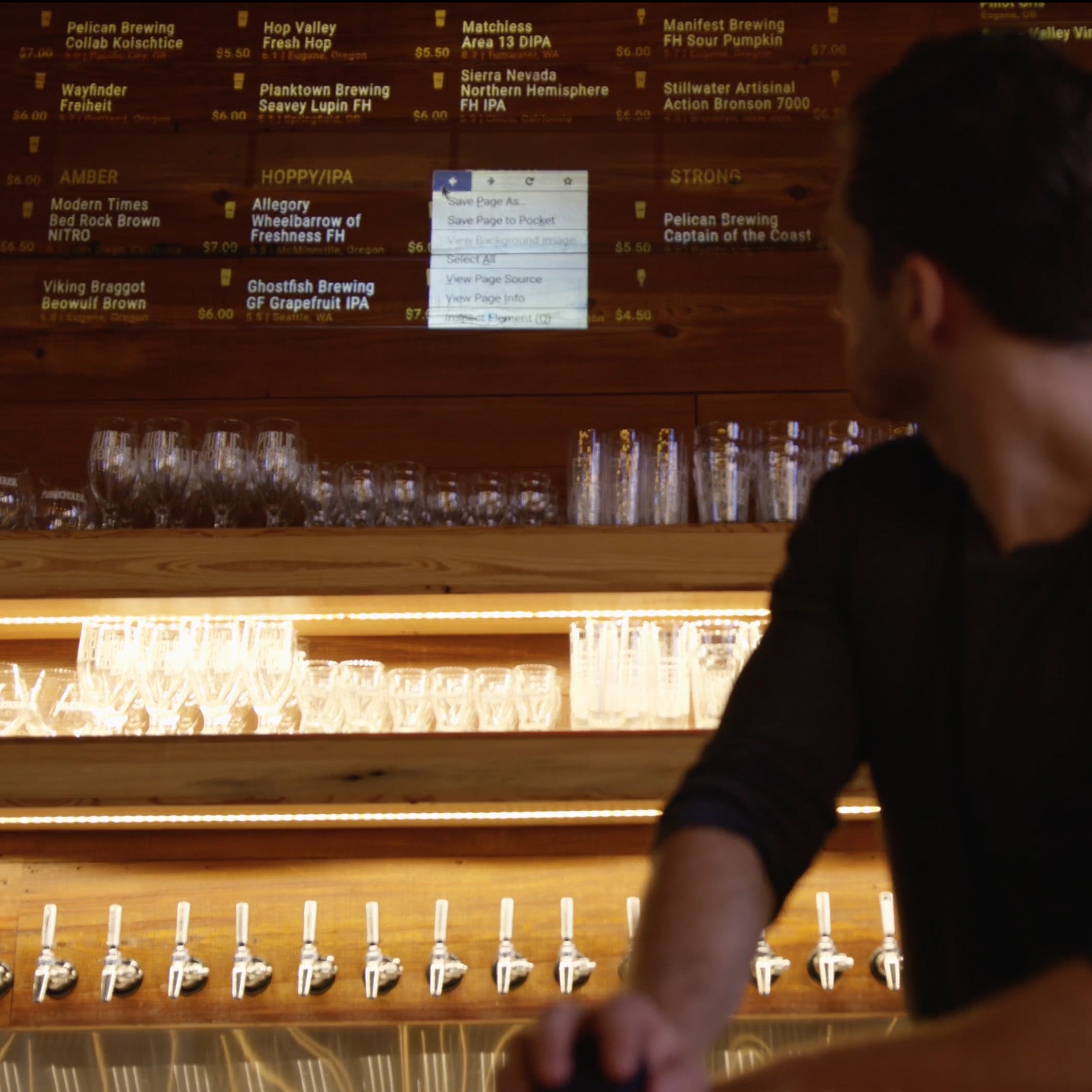 Man at a Public House taproom bar with a beer menu and browser menu projected on the wall