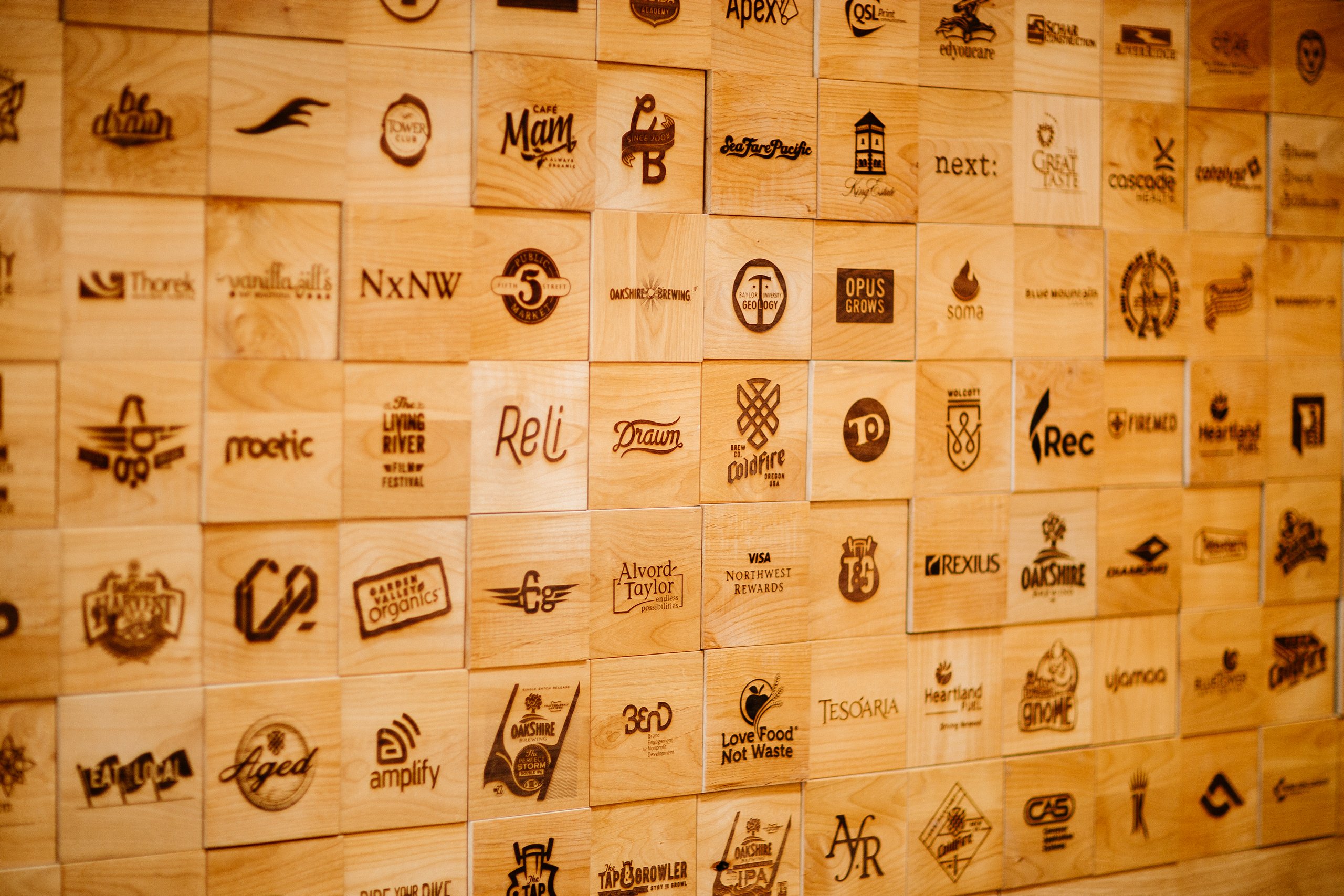 Wall of wood blocks laser-engraved with client logos including Drawn and Coldfire