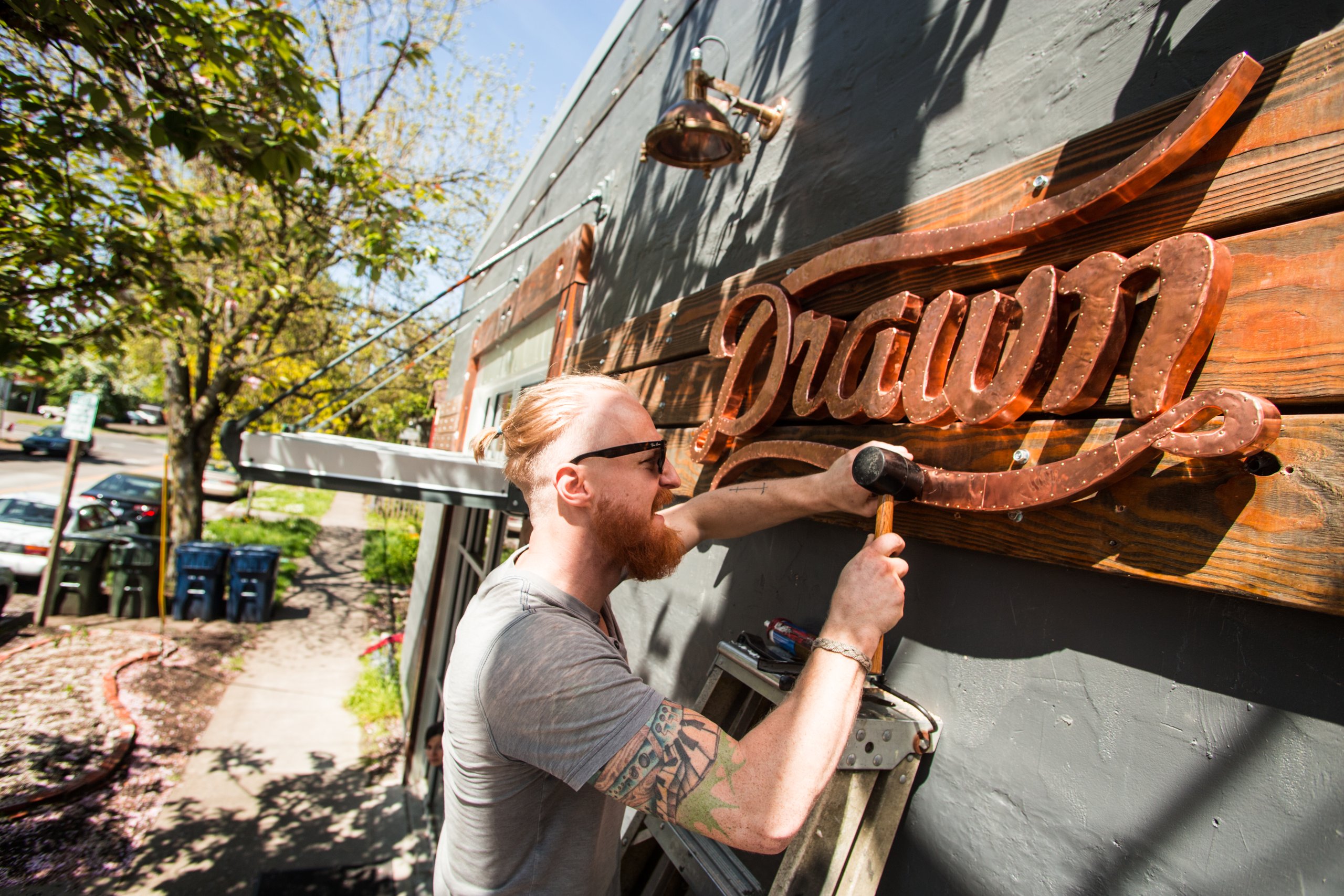 Man mounting a copper Drawn script sign on a wooden building facade
