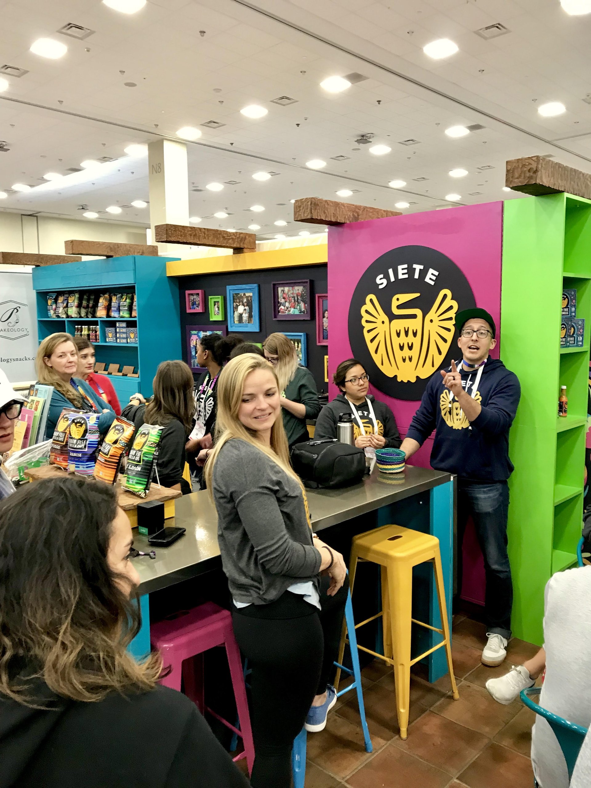 Siete trade show booth with pink logo wall and people gathered at a counter