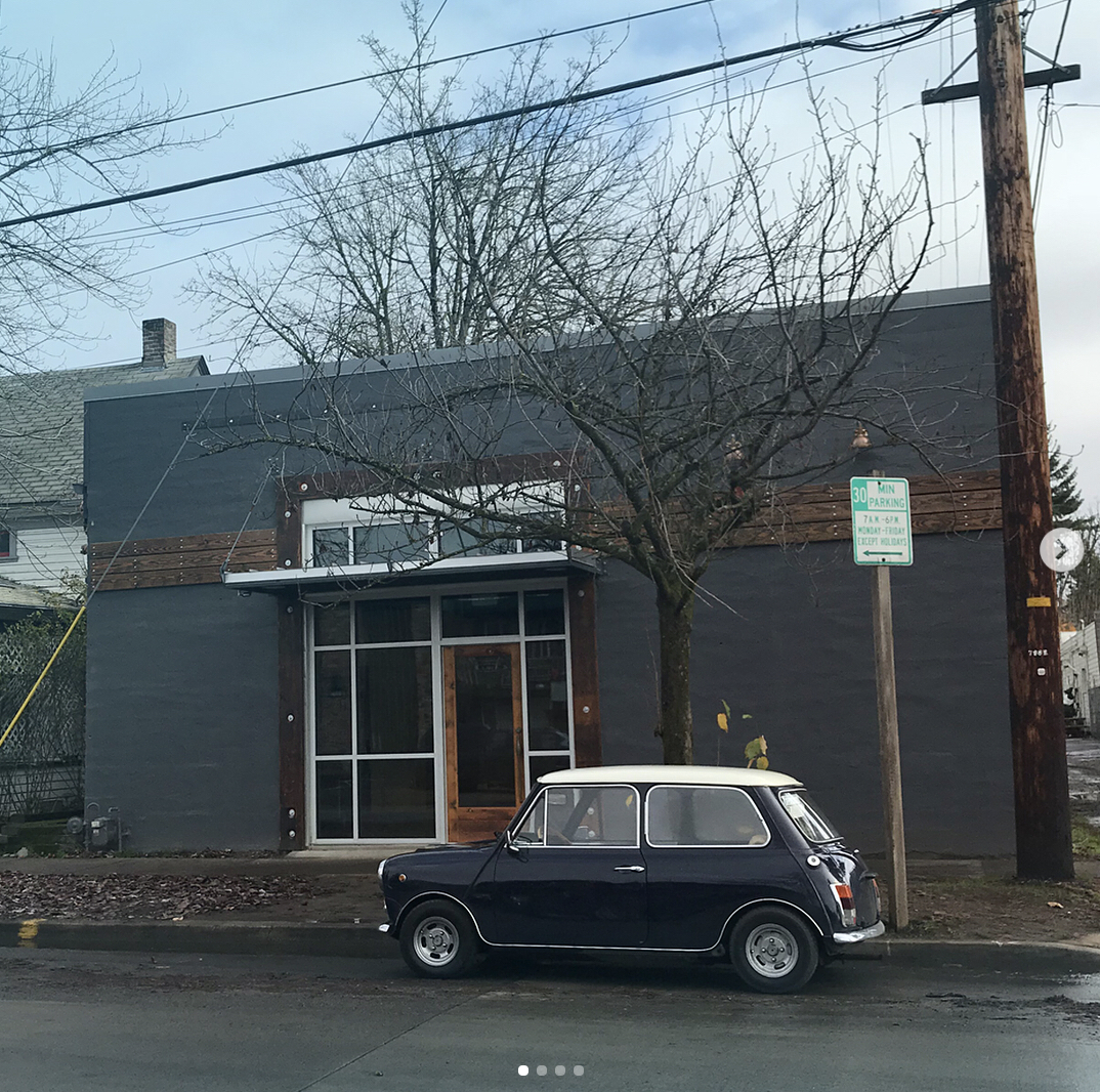 Gray storefront exterior with a vintage navy-and-white Mini Cooper parked out front