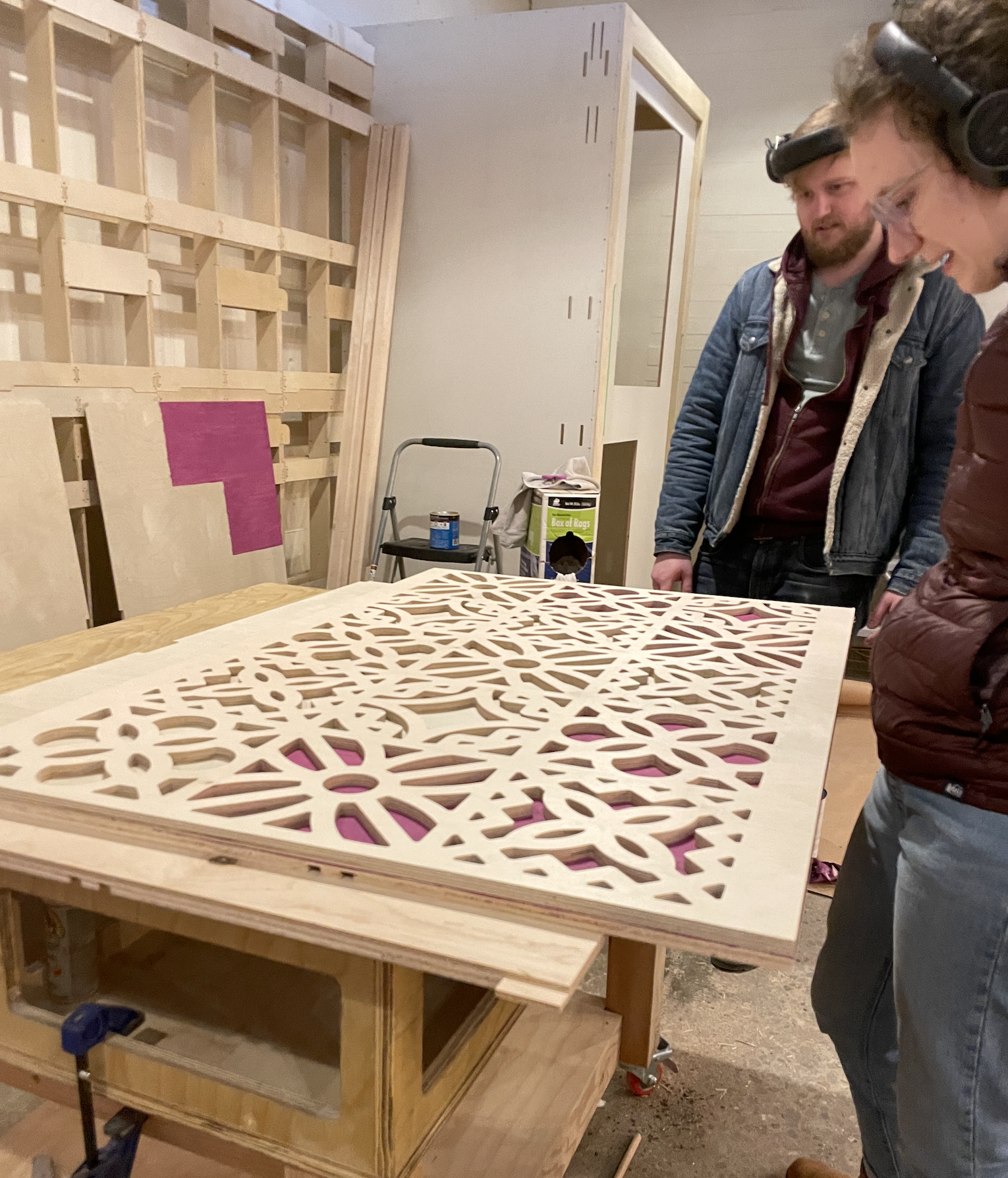 Two people in a workshop inspecting an intricate laser-cut wood lattice panel