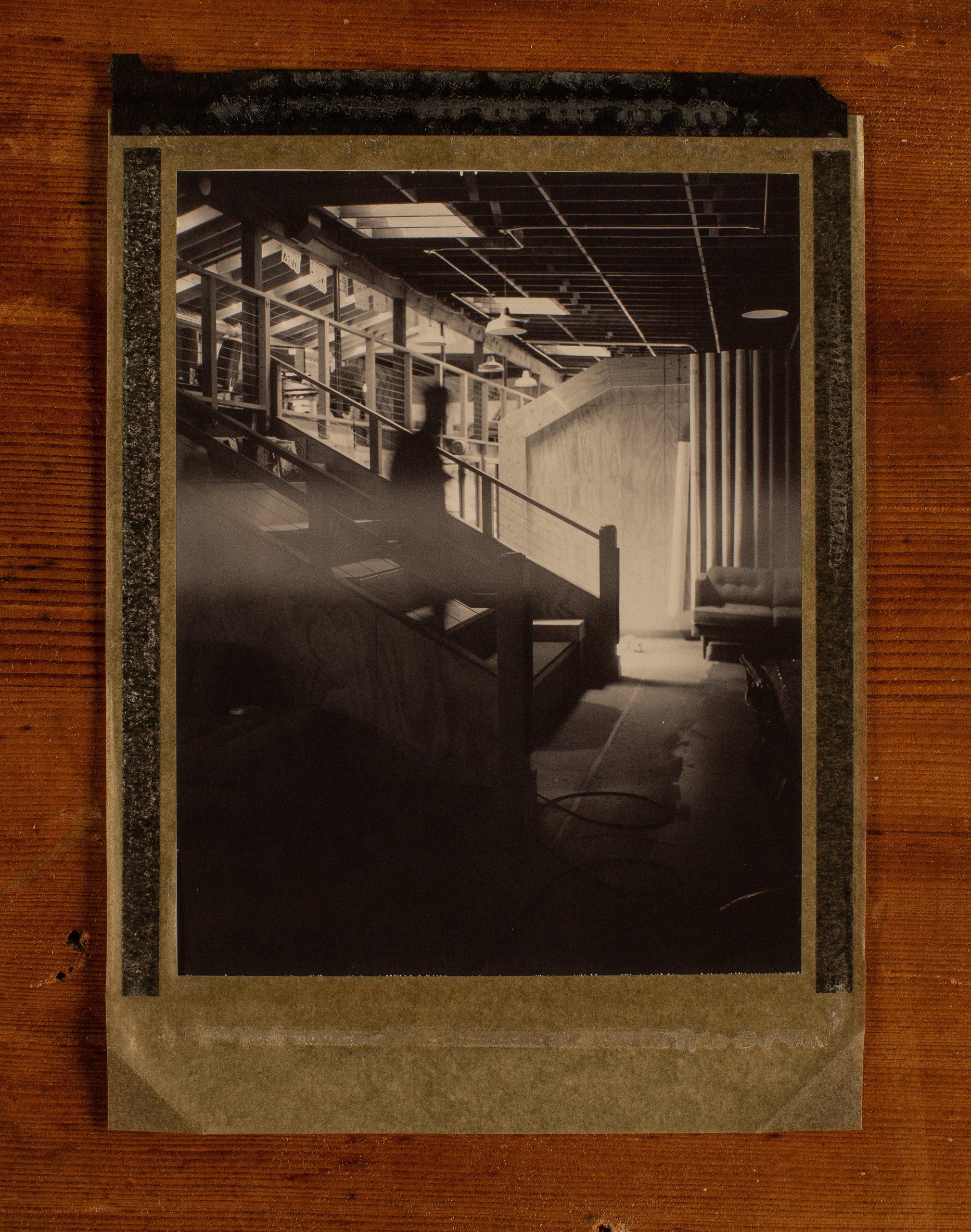 Black-and-white Polaroid taped to wood, blurred figure on a staircase in a loft office