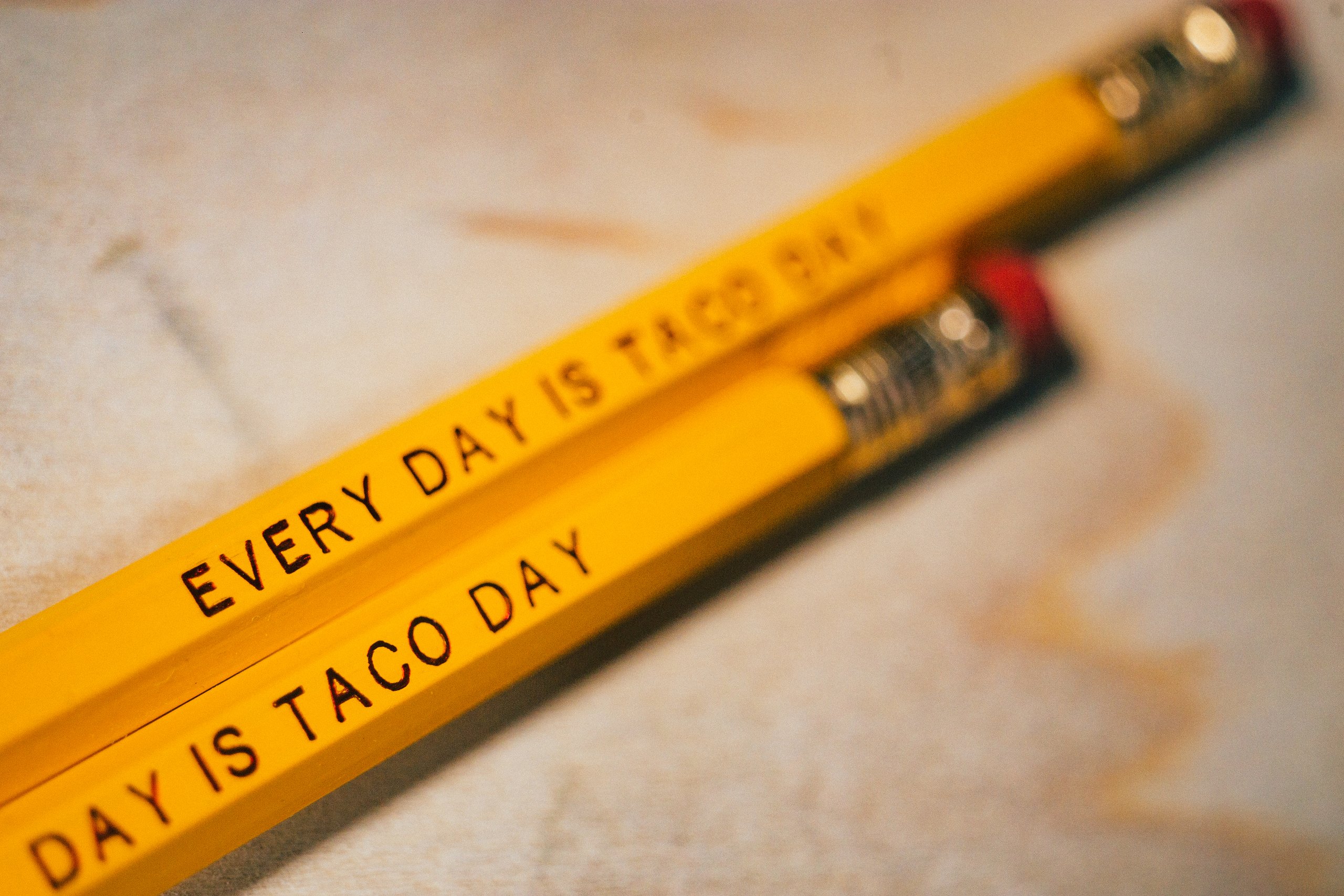 Two yellow pencils printed Every Day Is Taco Day on a wood surface