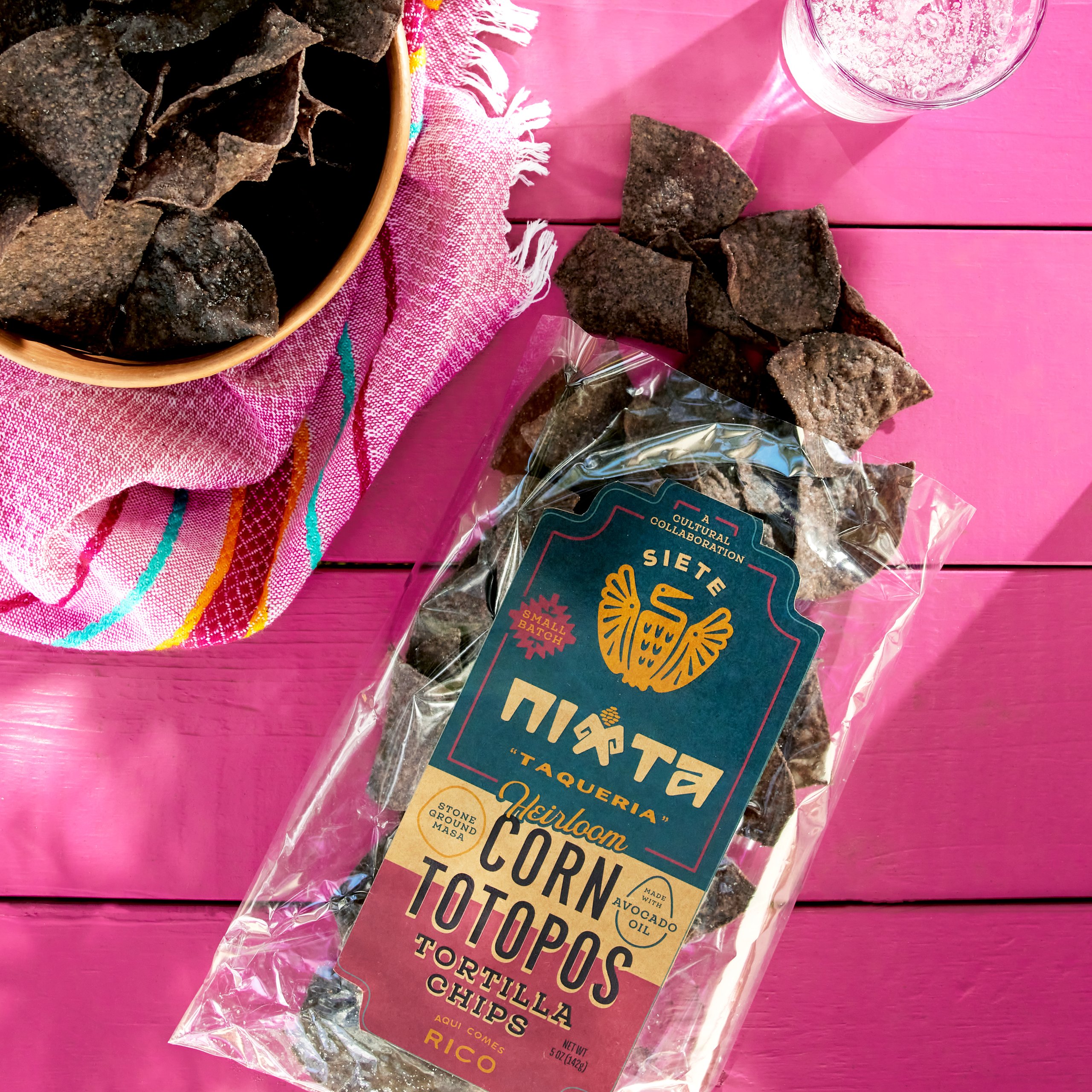 Siete x Nixta heirloom corn totopos chip bag with blue corn chips on pink table