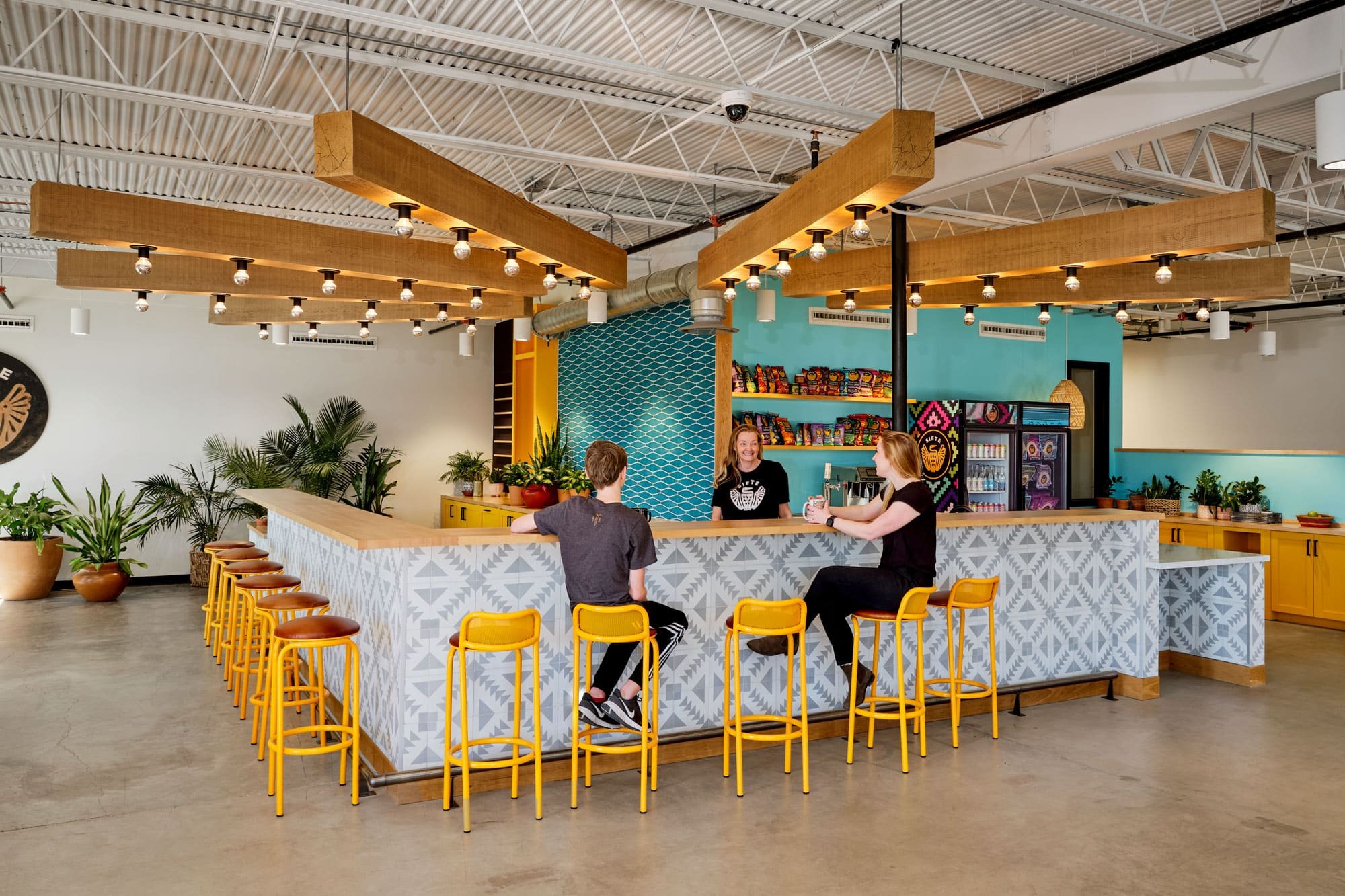 Siete office cafe bar with yellow stools, teal tile, and snack-lined shelves