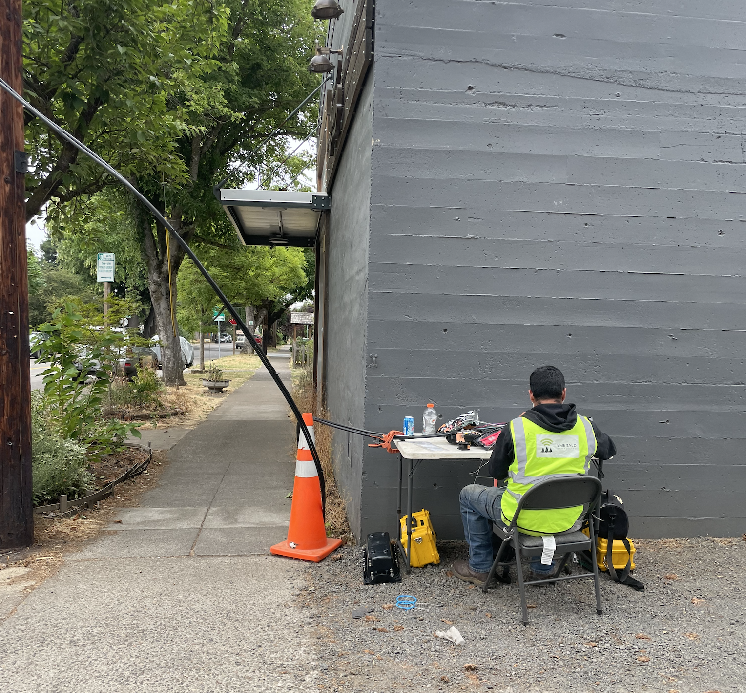Technician in yellow safety vest working on cabling at a folding table by a sidewalk