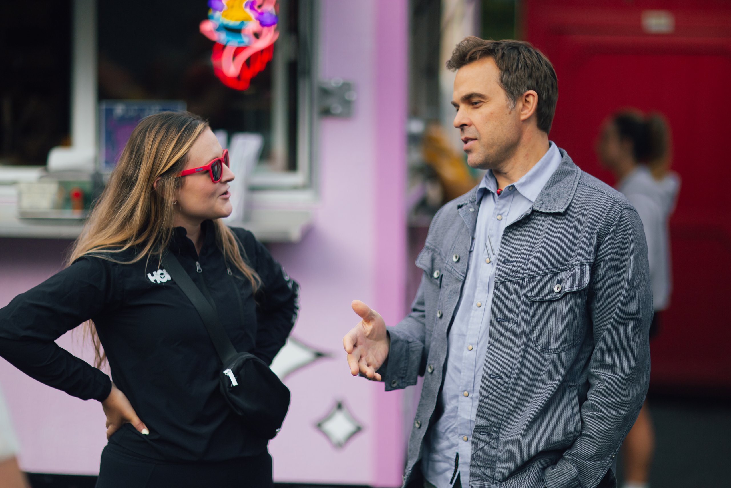 Woman in Hoka jacket and red sunglasses chatting with man beside a pink food truck