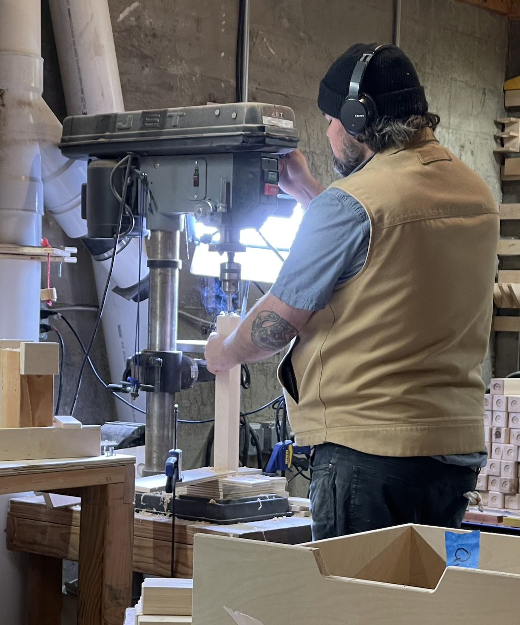 Worker in beanie and headphones using a JET drill press in a woodshop