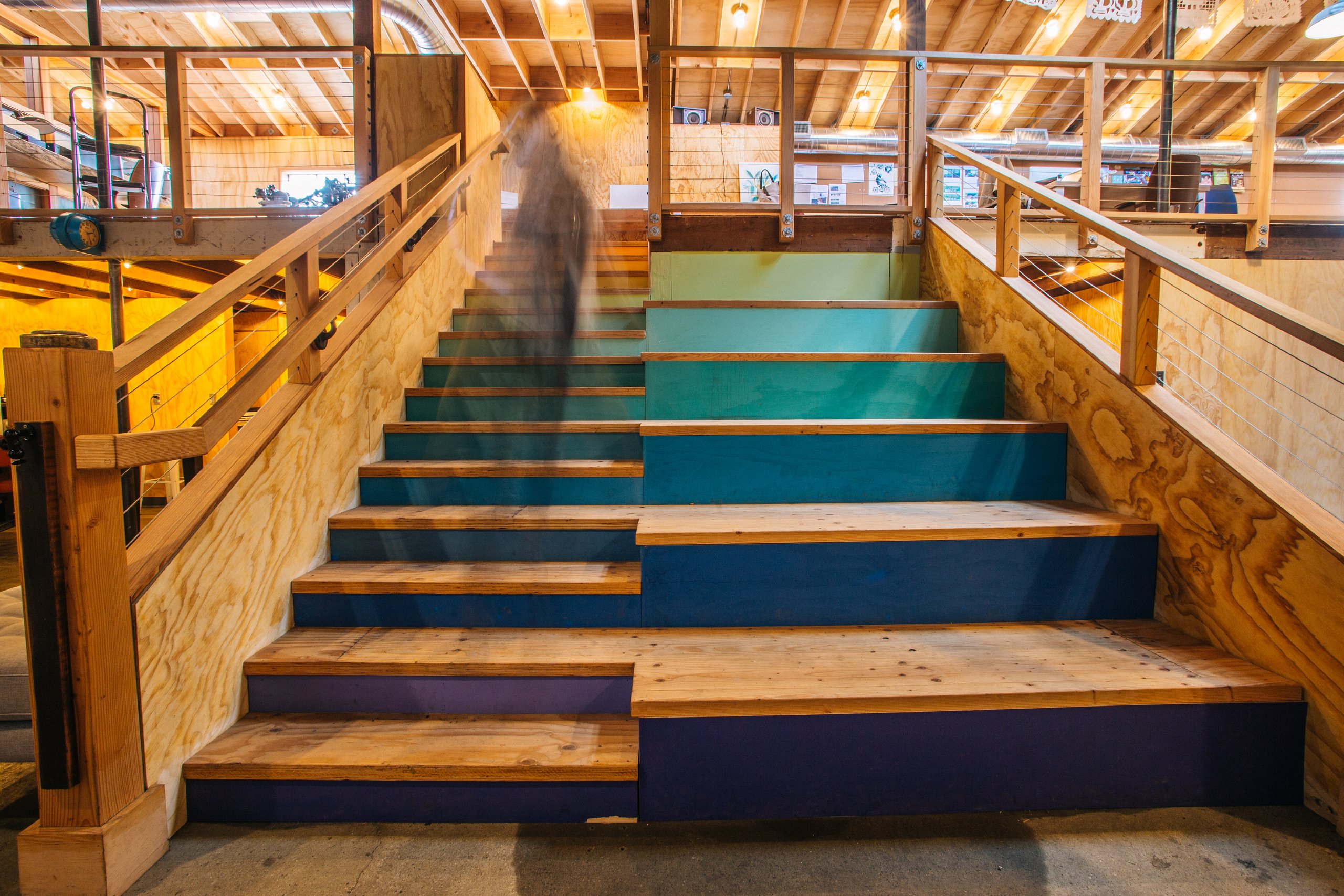 Person climbing a colorful ombre-painted wooden staircase in a wood-framed workshop
