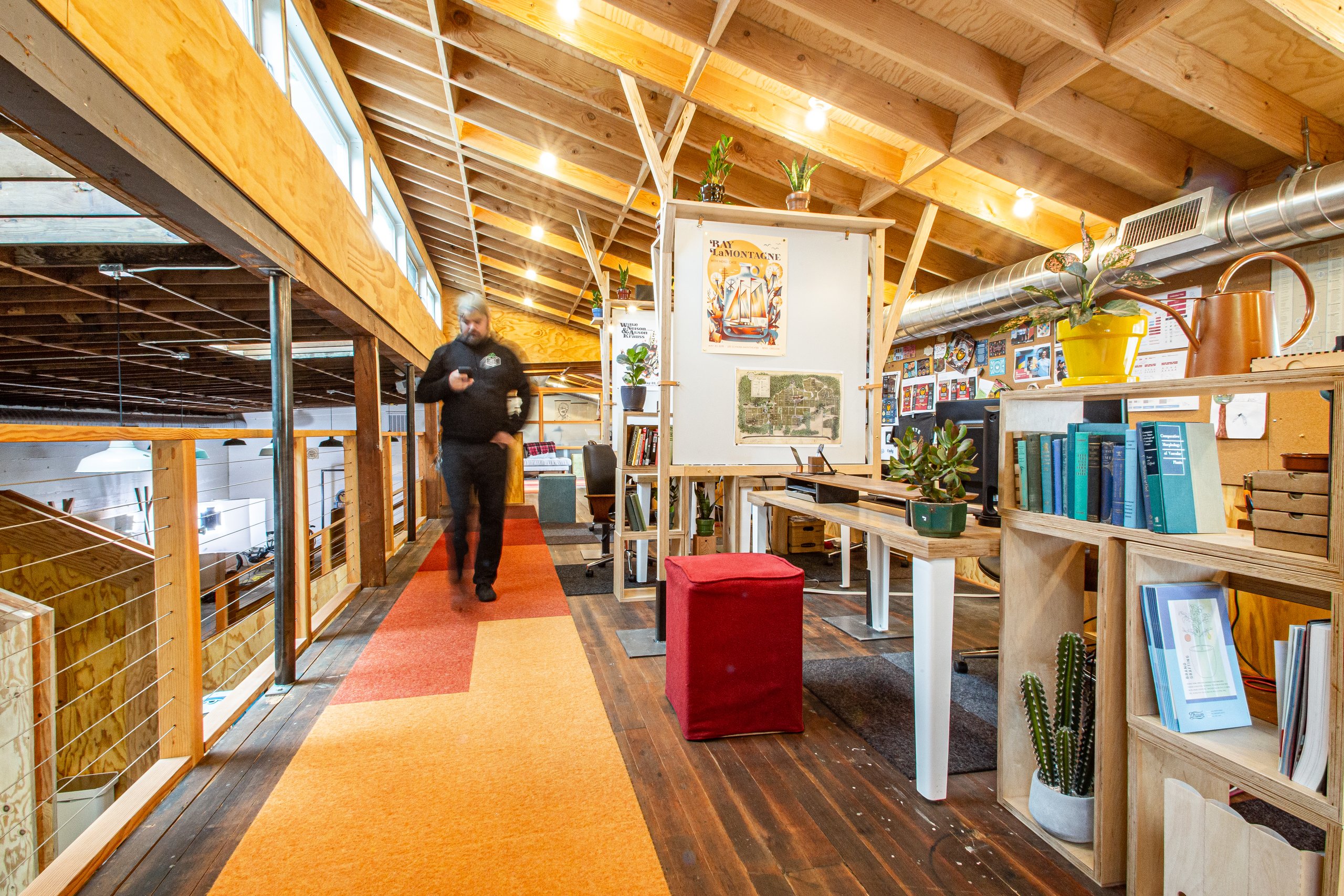 Man walking an orange runner through Drawn's wood-beamed studio loft with plants and bookshelves