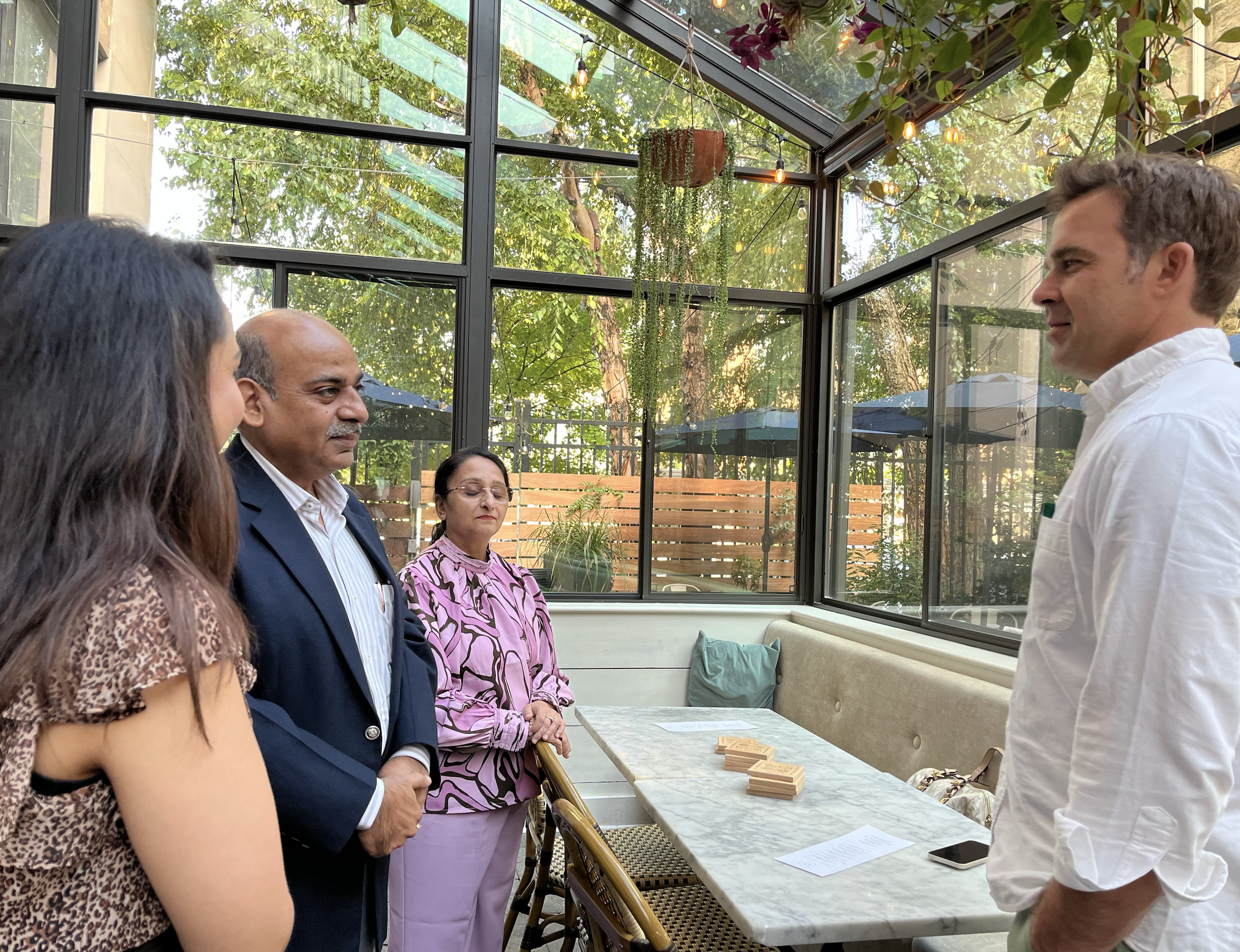 Four people talking in a plant-filled glass conservatory restaurant