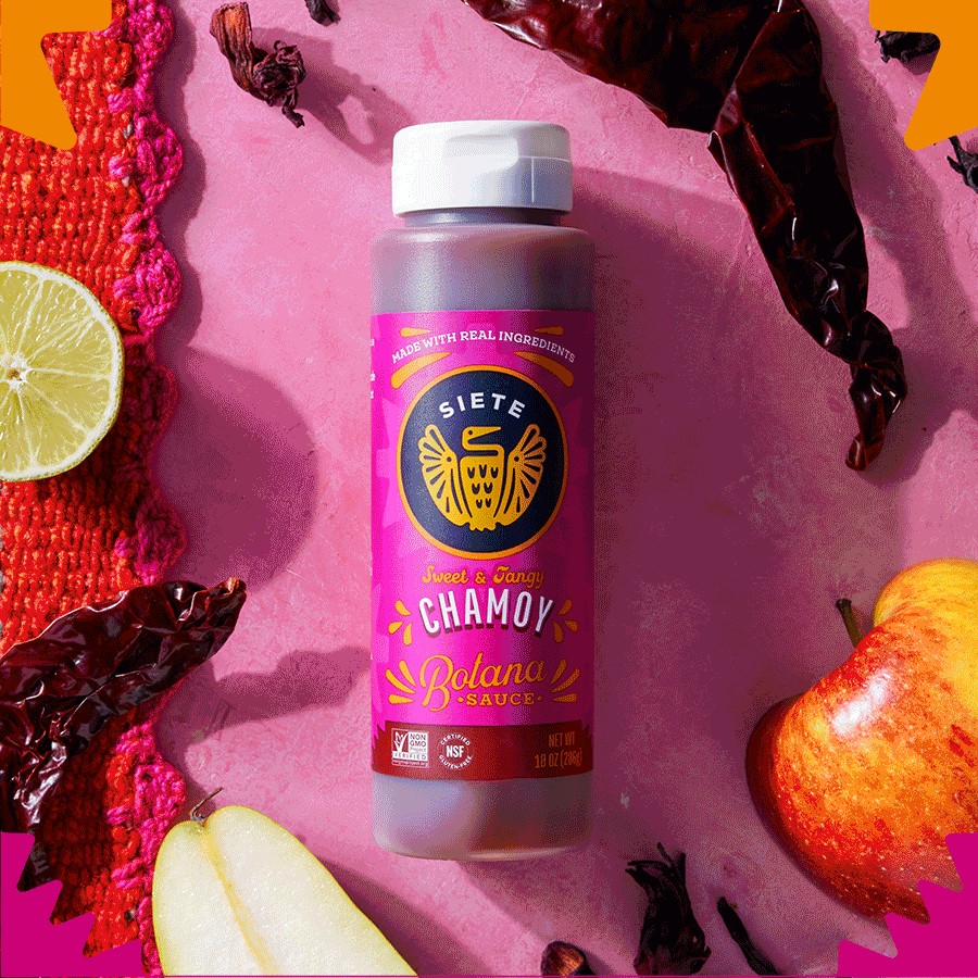 Siete Chamoy Botana Sauce bottle on pink backdrop with dried chiles, lime, and apple
