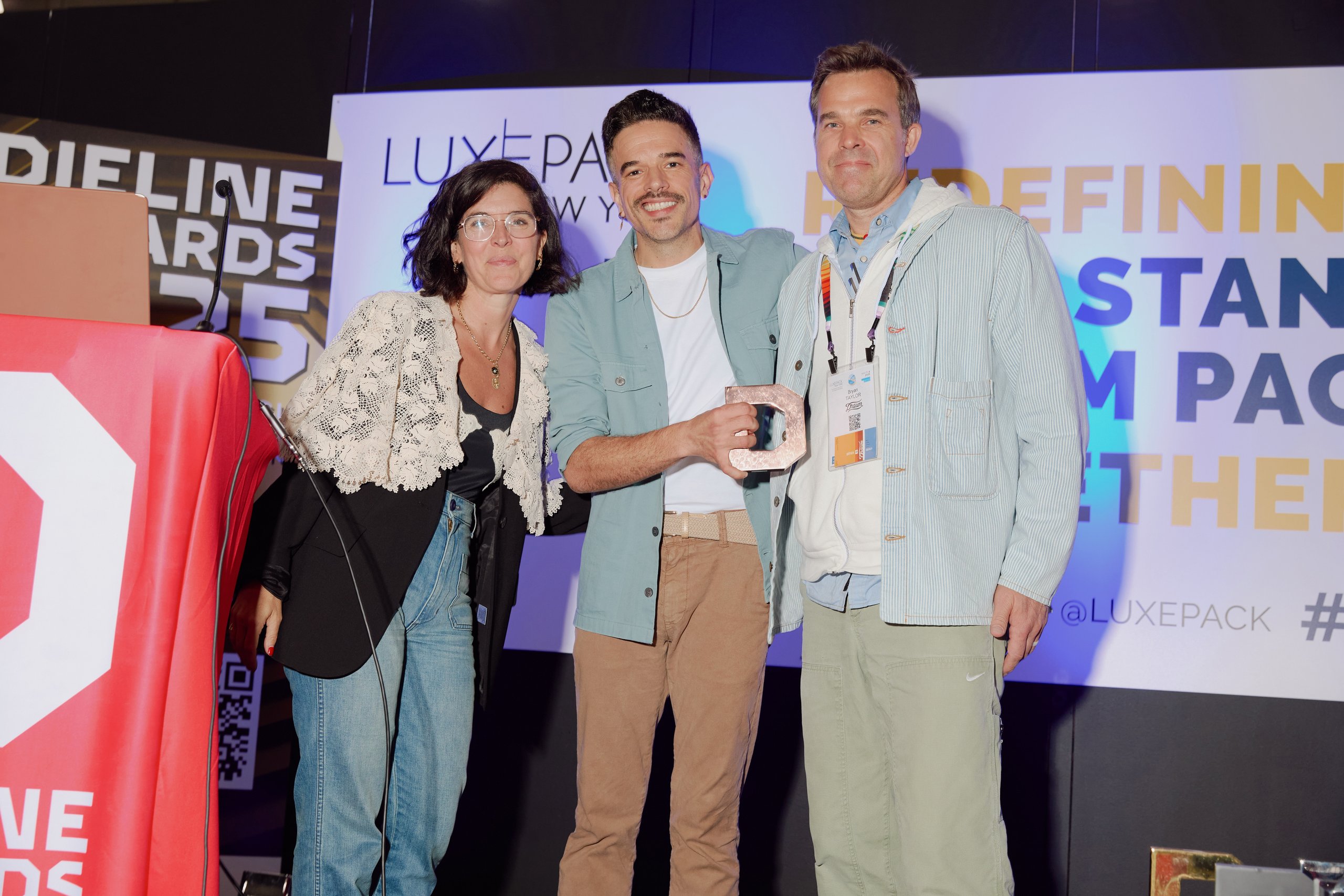 Three people holding a copper trophy onstage at the Dieline Awards, LUXE PACK New York
