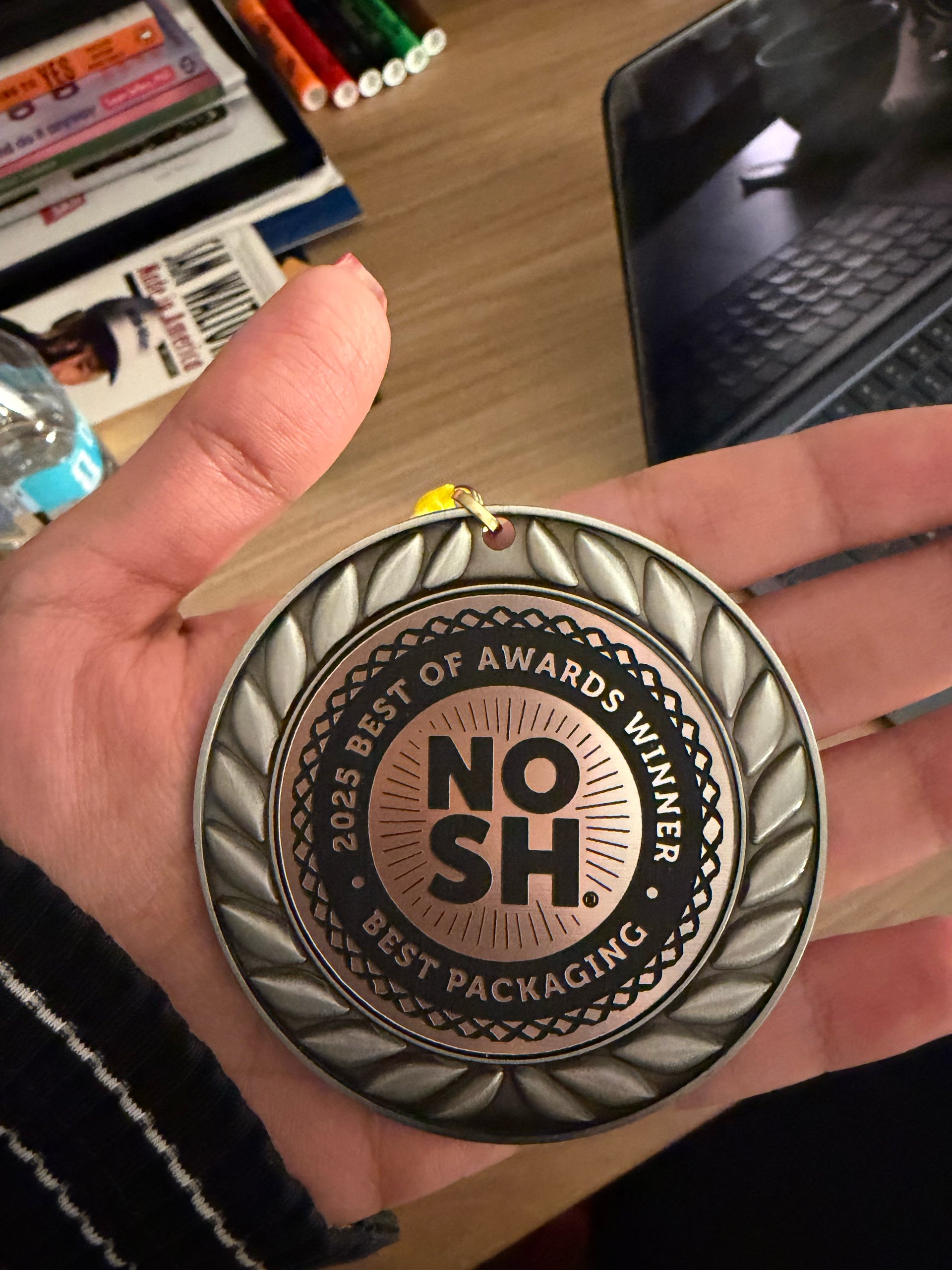 Hand holding a NOSH 2025 Best of Awards Winner medal for Best Packaging