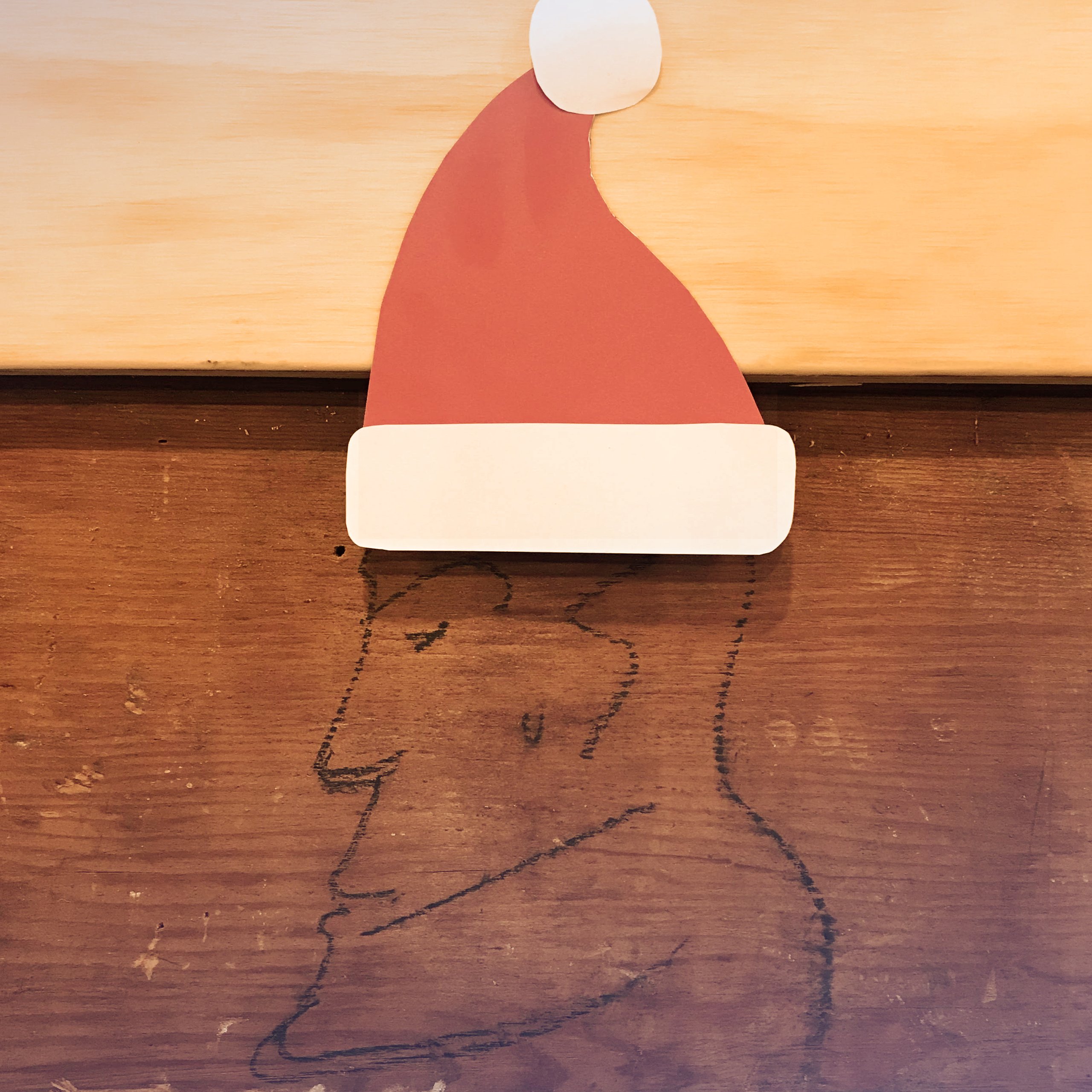 Paper Santa hat cutout above a pencil sketch of Santa's bearded face on wood