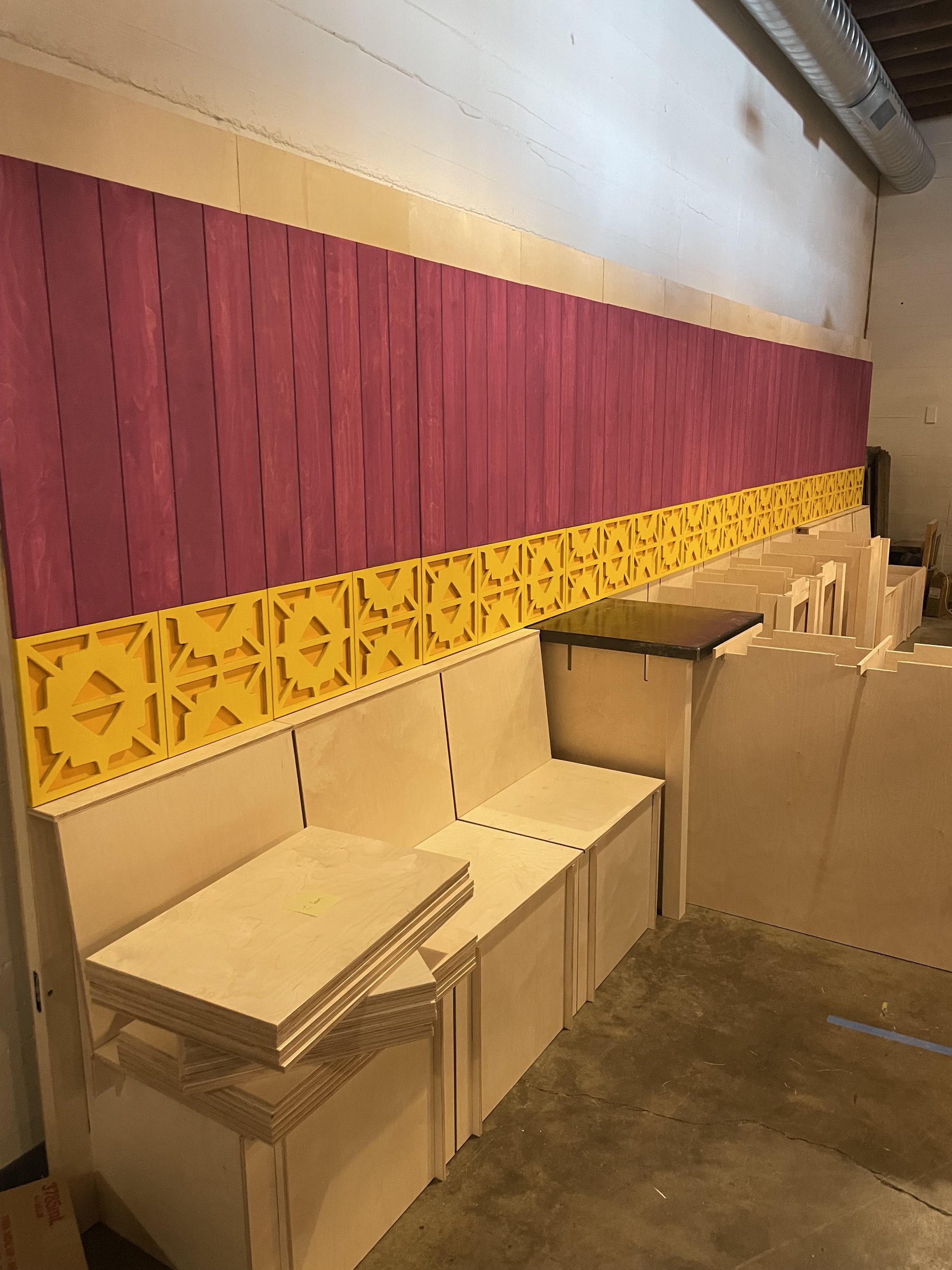 Siete trade-show booth being built: plywood benches, magenta wall, yellow geometric cutout panels
