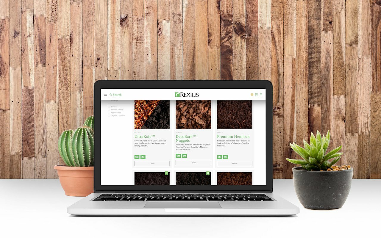 Laptop showing the Rexius Shopify store with mulch and soil products, flanked by potted succulents