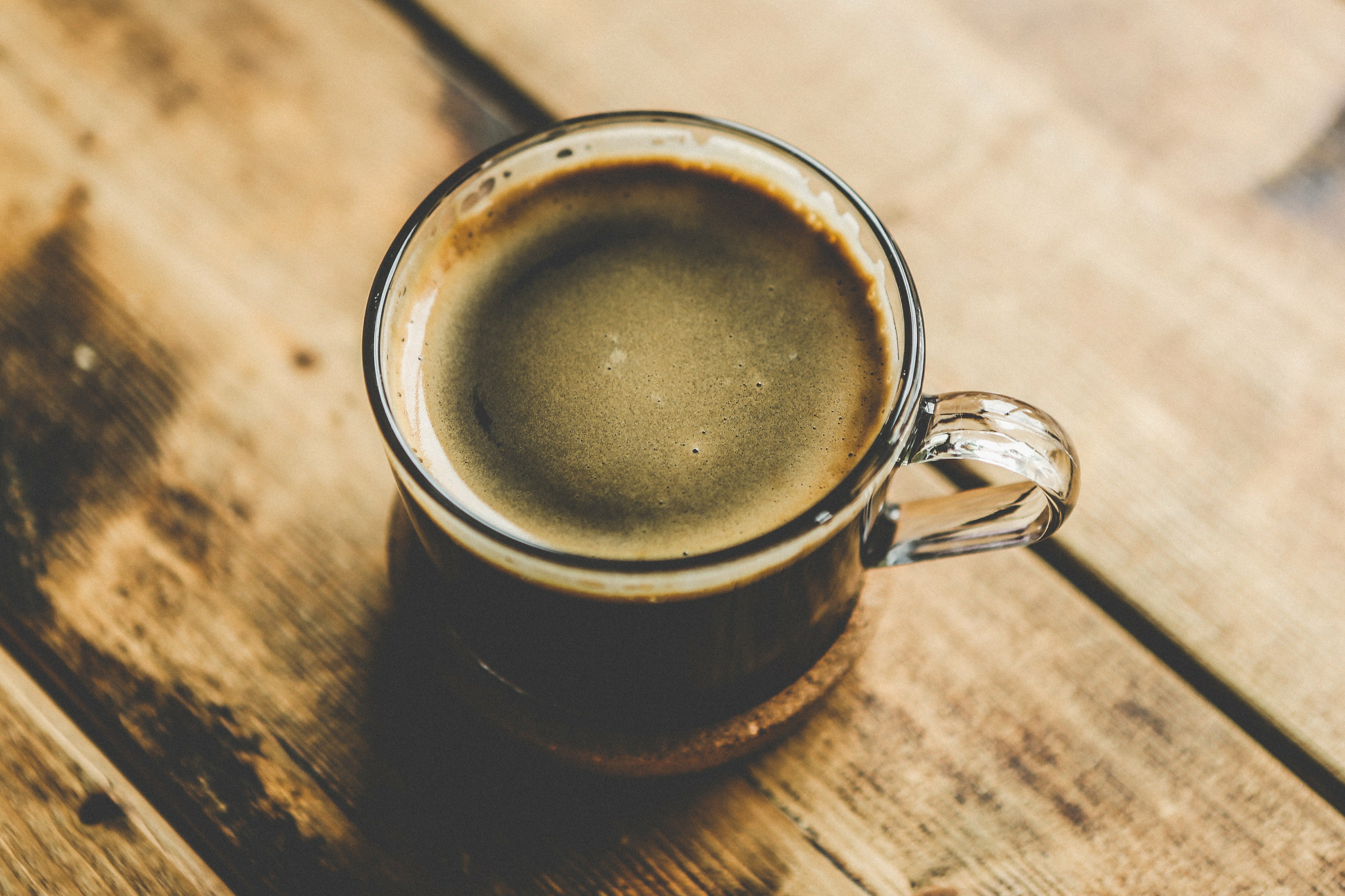 Glass mug of frothy coffee on a rustic wooden table