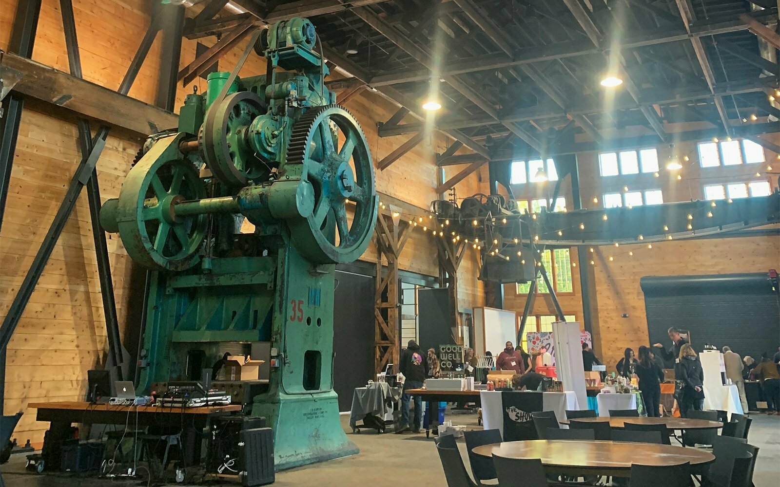 Vintage green industrial press machine inside the timber-framed Built Oregon Festival venue with string lights