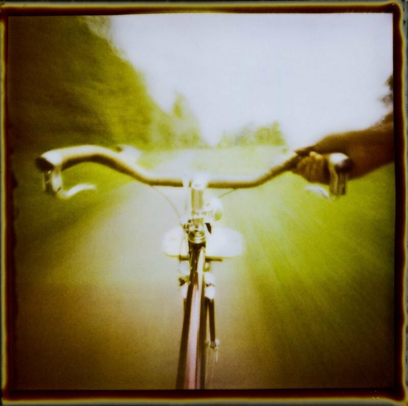 Blurred first-person view over bicycle handlebars riding down a path, by Trask Bedortha