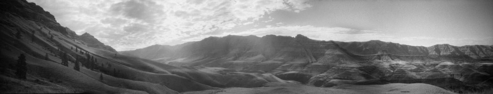 Black-and-white panorama of mountains and rolling hills under a hazy sky by Trask Bedortha