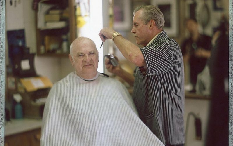 Barber cutting an older man's hair in a salon, photographed by Trask Bedortha