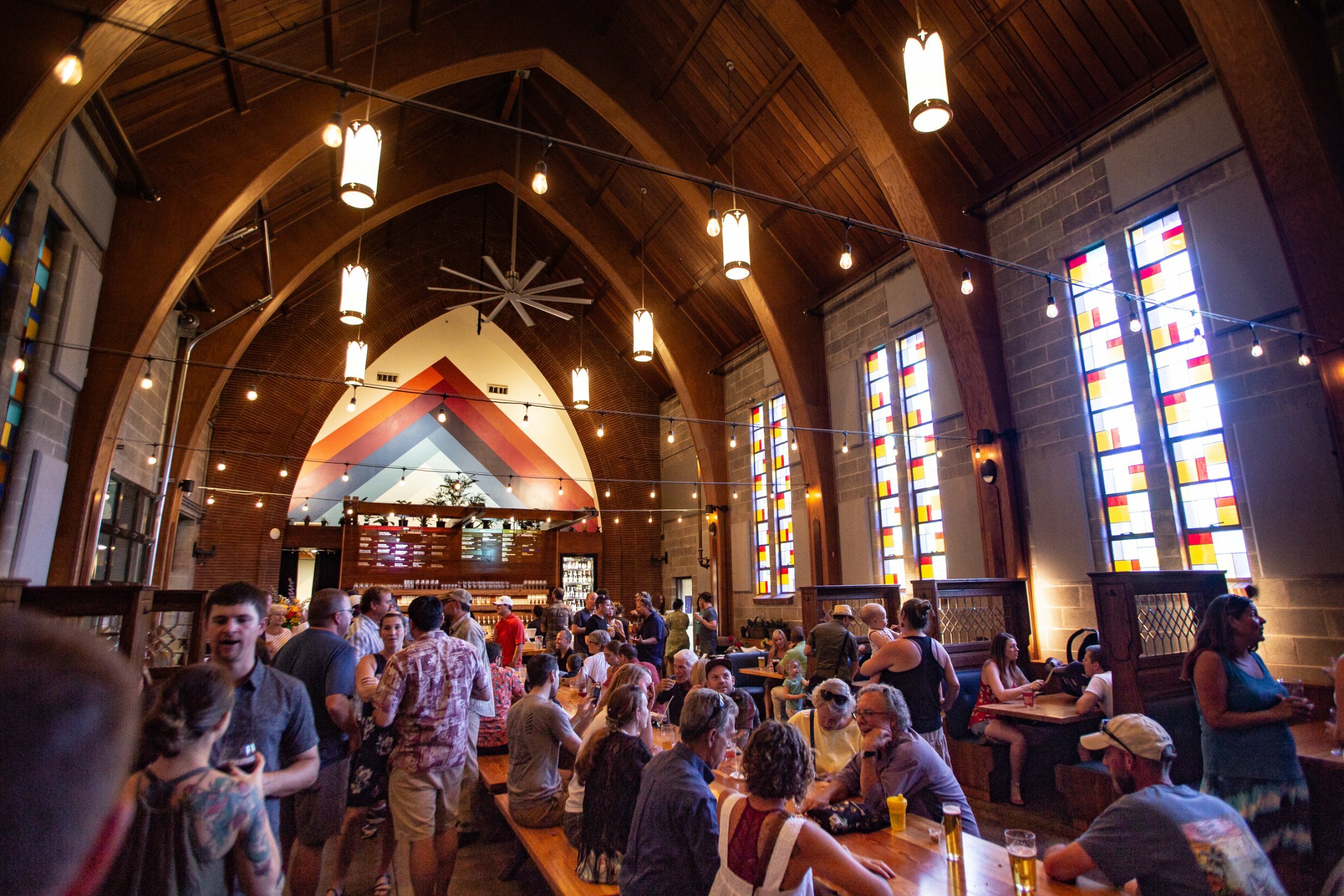 Vaulted arched ceiling and stained-glass windows of the church converted into PublicHouse food hall, filled with patrons