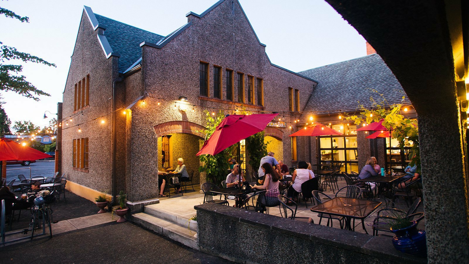 Stone church exterior of PublicHouse at dusk with red umbrellas and string lights over the outdoor patio