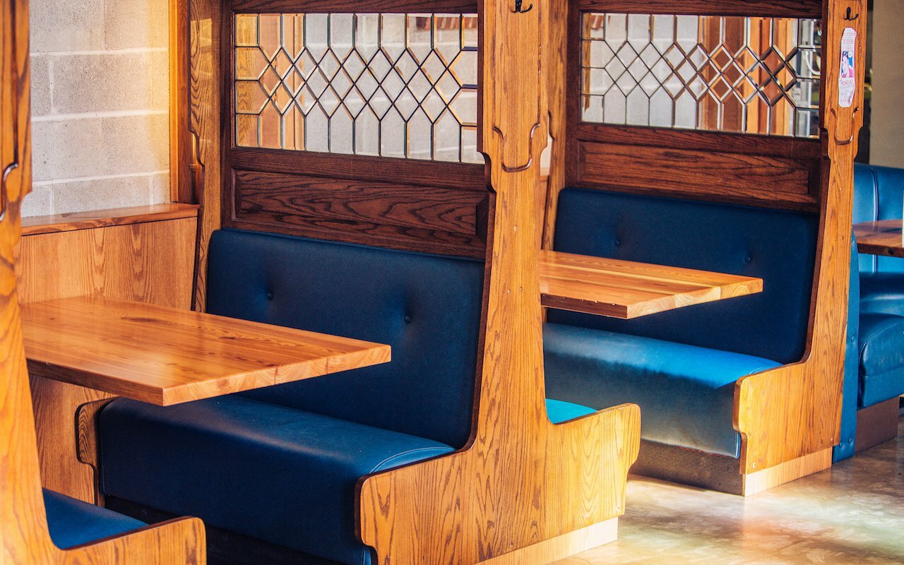 Wooden booths with blue leather seating and leaded-glass dividers inside PublicHouse food hall