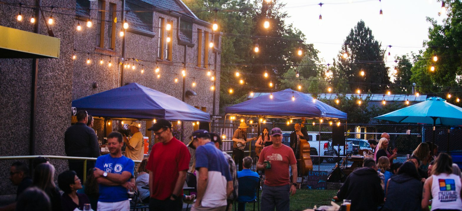 Evening crowd under string lights and tents at PublicHouse outdoor patio beside the stone church building
