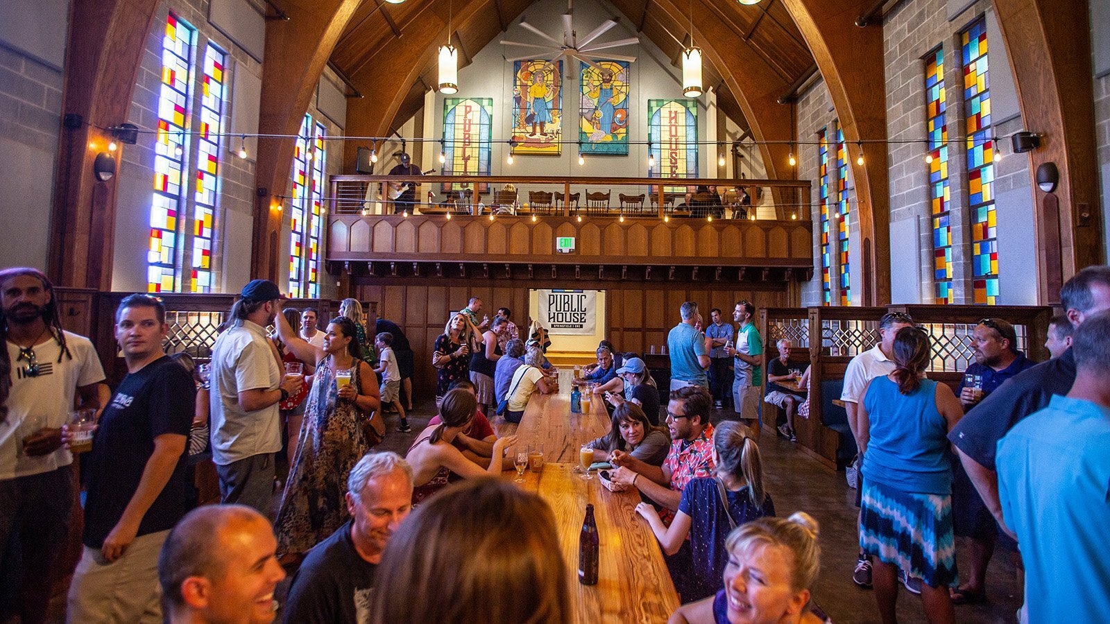 PublicHouse food hall crowd at communal tables inside a converted church with stained-glass windows