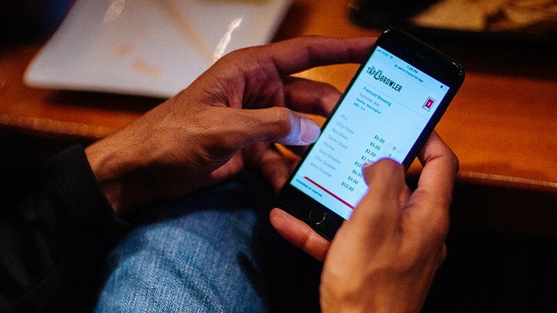 Hands using the Growler ordering app on a phone showing a menu at a restaurant table