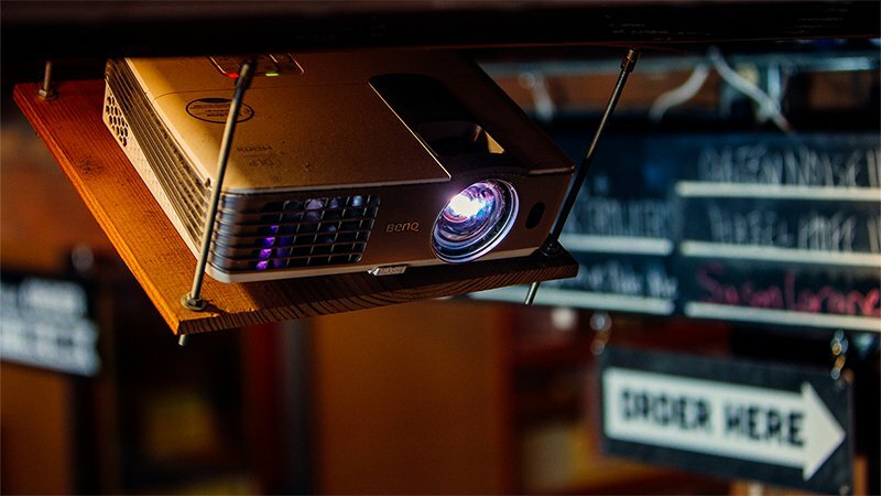 BenQ projector mounted under a shelf projecting toward menu boards, near an Order Here arrow sign