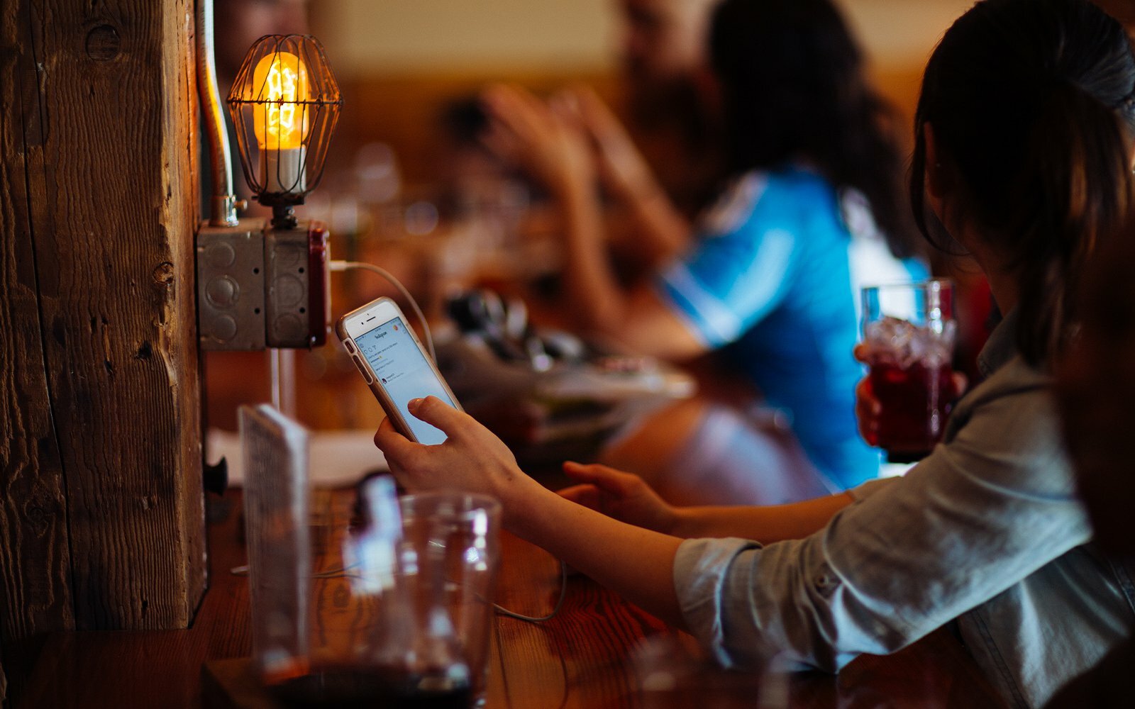 Diner using the Porter app on a phone at a restaurant bar lit by a warm Edison bulb lamp