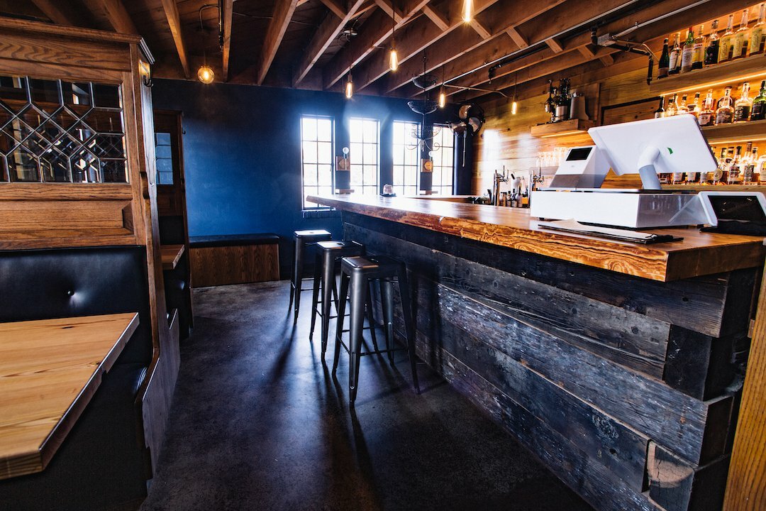 Drawn-designed pub interior with reclaimed-wood bar, point-of-sale terminal, stools and dark blue walls