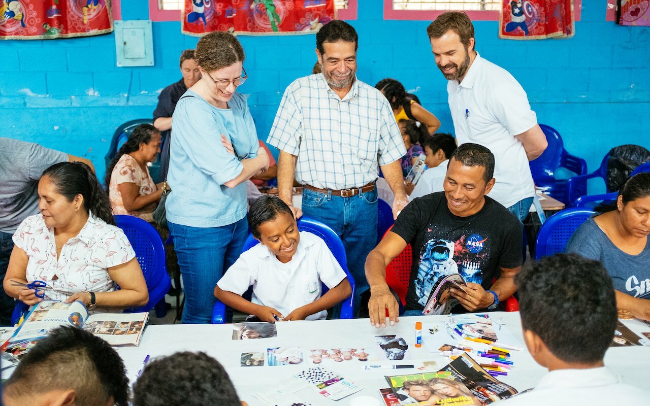 Drawn team members and locals making collages together at tables in a blue El Salvador classroom