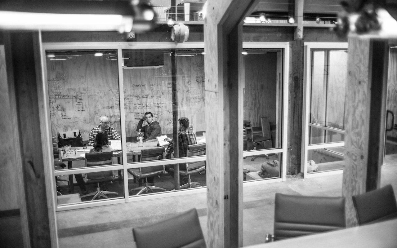 Black and white view through glass into Drawn's meeting room with team working at a table