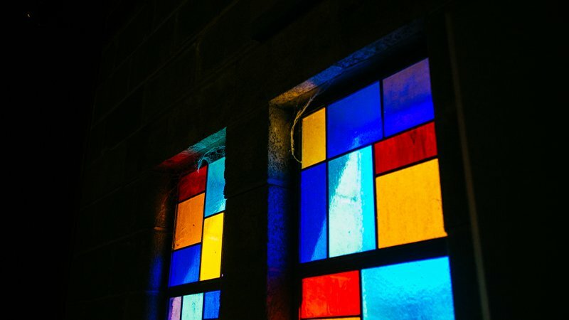 Stained glass window with colorful red, blue, yellow and orange panes against a dark wall