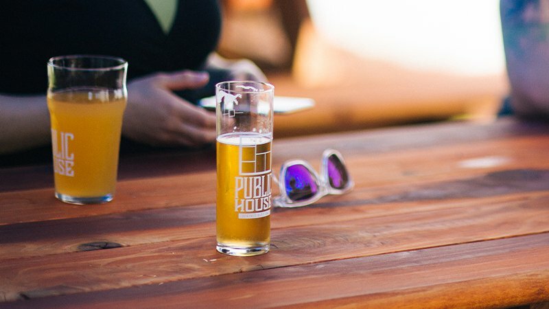 Two beer glasses etched with the Public House logo and sunglasses on a wooden table