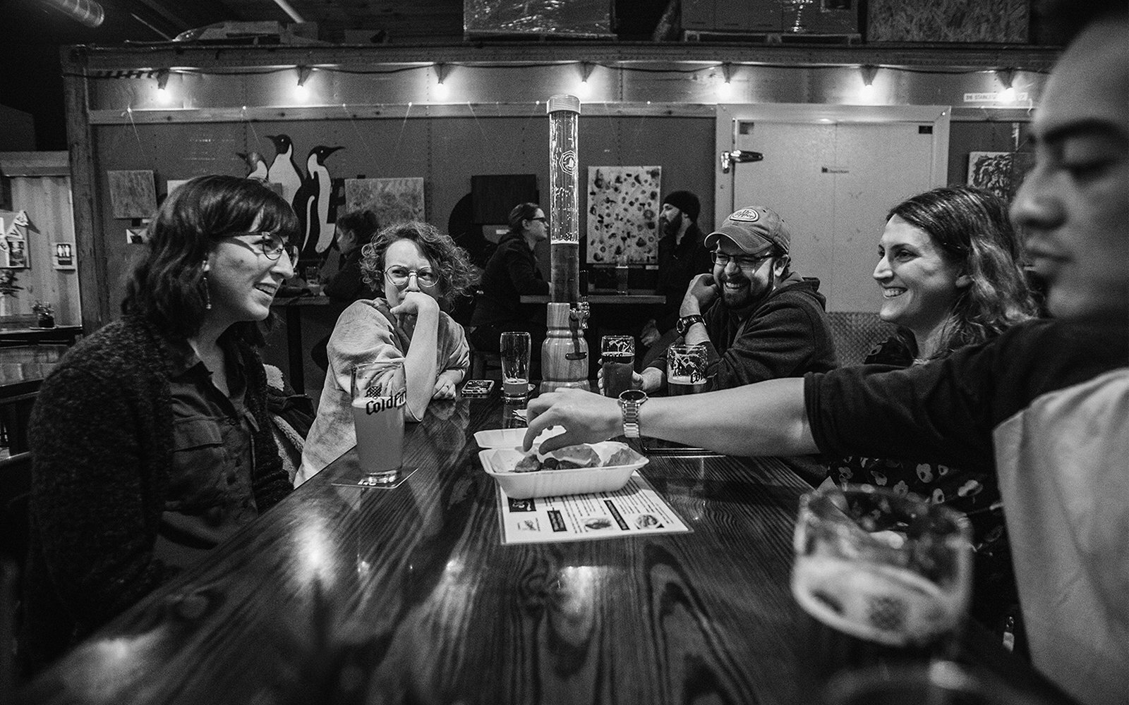 Friends laughing together at a bar, black and white, penguin artwork on the back wall