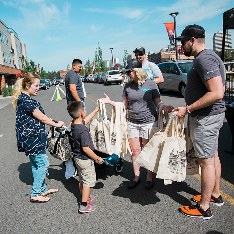 WSECU volunteers in branded shirts handing out tote bags to families on a sunny street